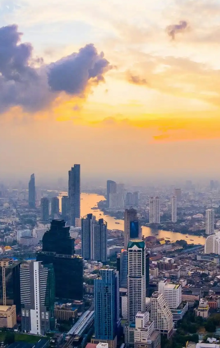 Urban skyline at sunset with high-rise buildings and a river winding through the city.