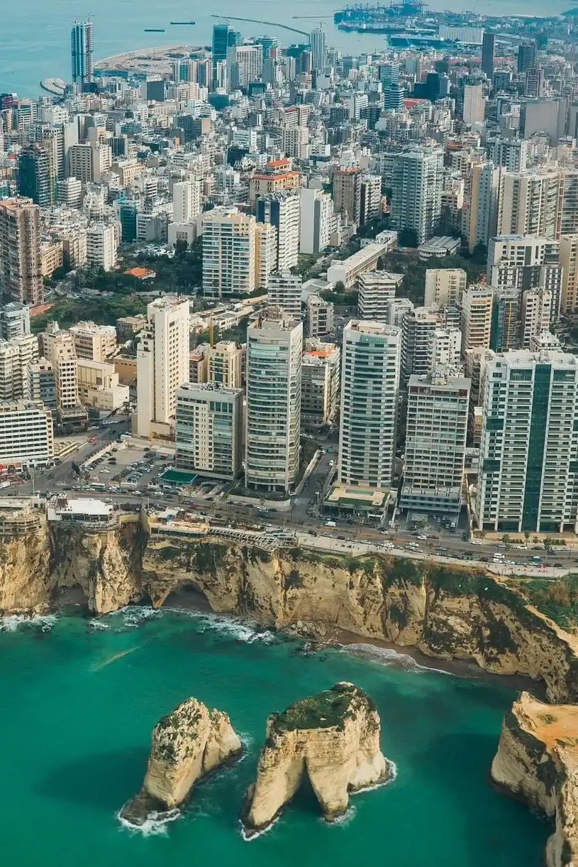 Aerial view of a coastal city with dense high-rise buildings and limestone rock formations in turquoise water.