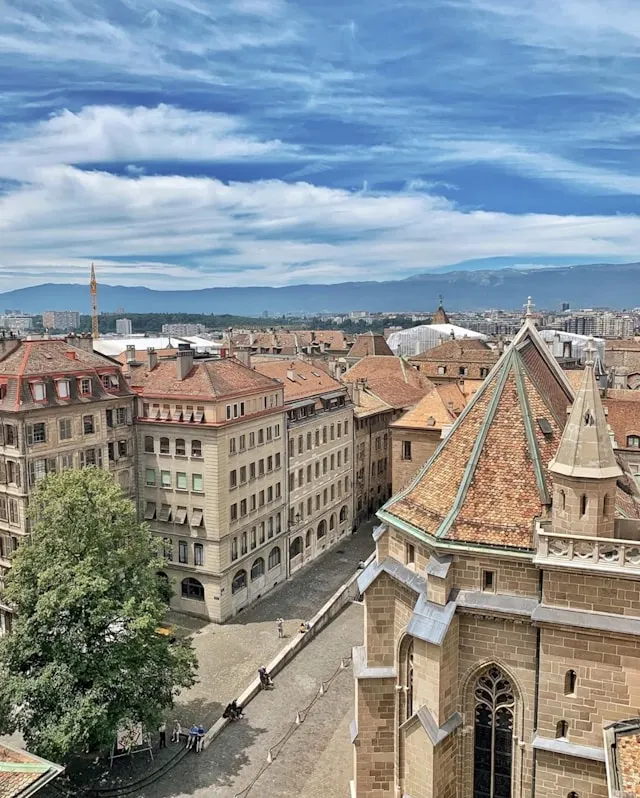 View over historic buildings with tiled roofs and a church tower under a partly cloudy blue sky.