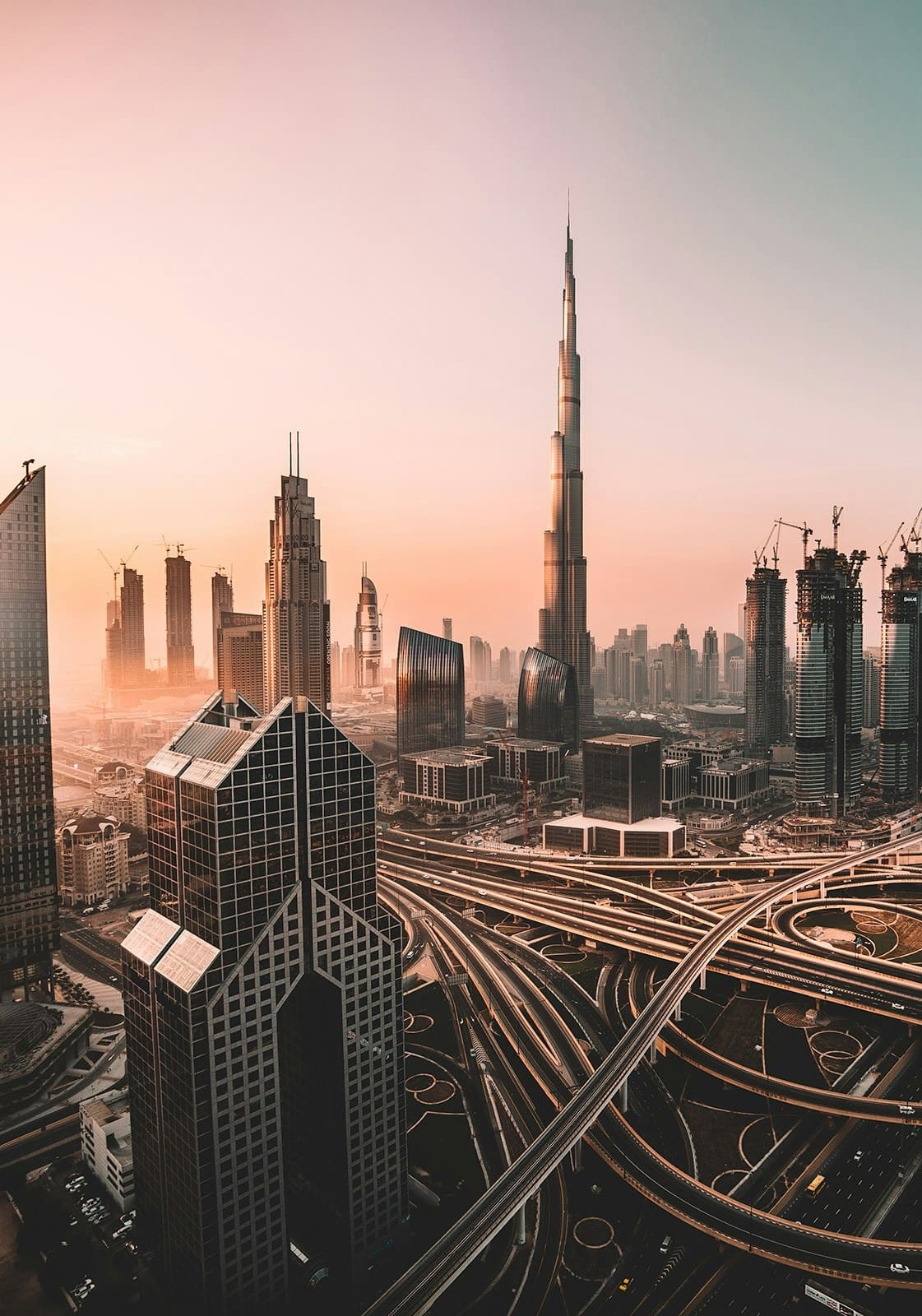 Aerial view of Dubai skyline at sunset with Burj Khalifa and interconnected highways in the foreground.